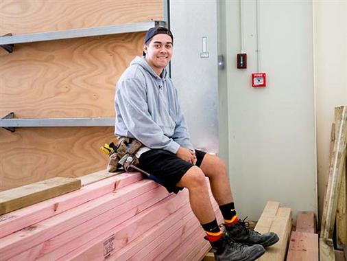 A young man sitting on a pile of timber in a workshop