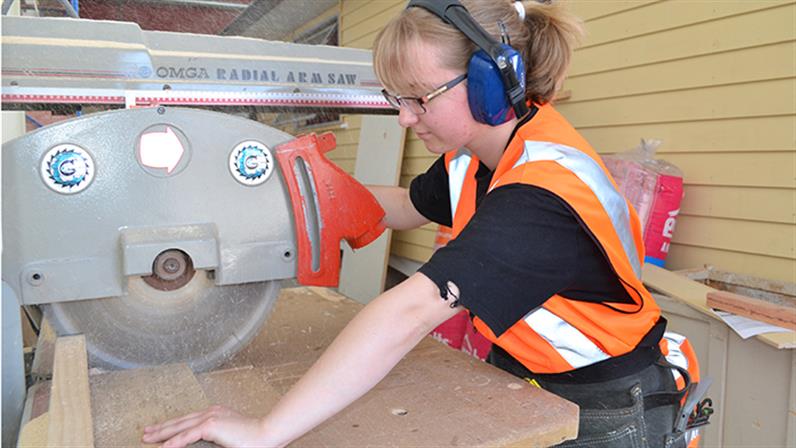 A young lady working on a skill saw in a workshop at UCOL 