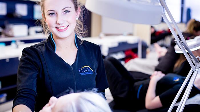 A girl smiling next to a ring light in a beauty therapy room