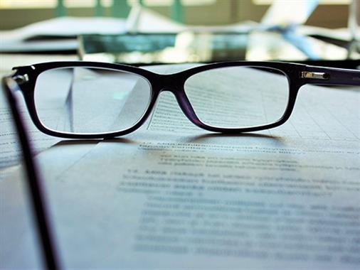 A close up photograph of a contract with a pair of prescription glasses sitting on it