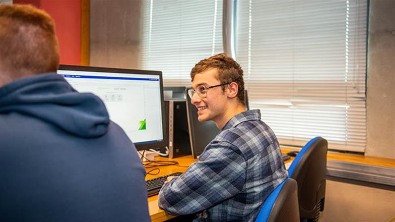 A photograph of a happy student in front of a computer