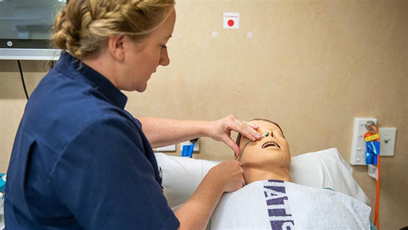 A photograph of a nursing student administrating a dummy patient