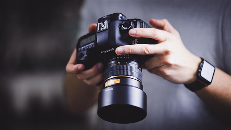 A close-up photograph of a DSLR camera in a student's hands