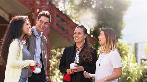 A photograph of a group of people chatting in front of a marae