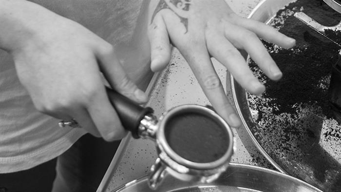 A close up photograph of a person's hands tamping coffee grinds