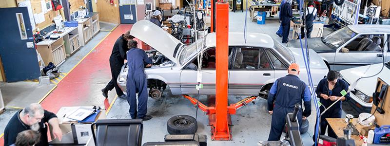 A photograph of the automotive workshop at UCOL in Palmerston North featuring students and lecturers working on cars and equipment