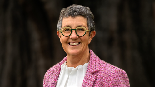 Leanne Southey smiles into the camera wearing a pink jacket with a dark neutral background