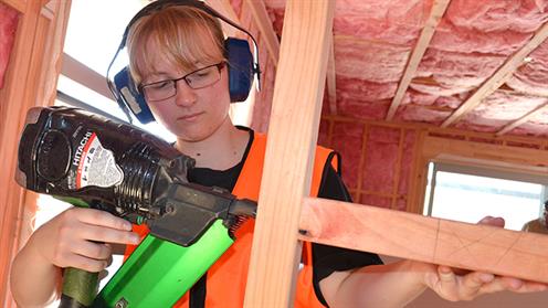 A photograph of a young lady using a nail gun to construct a wall in a house
