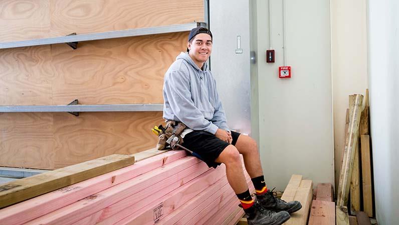A carpentry student sitting on a pile of timber