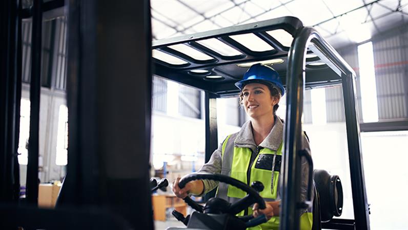 A photograph of a woman driving a forklift