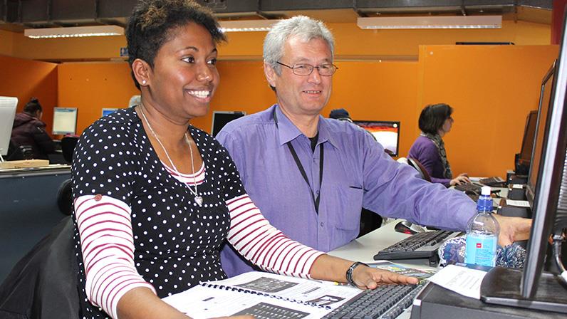 A photograph of a lecturer instructing a lady at the computer lab