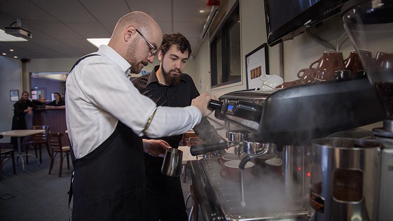 A photograph of the hospitality lecturer Niels Huibers showing a student how to make the perfect coffee
