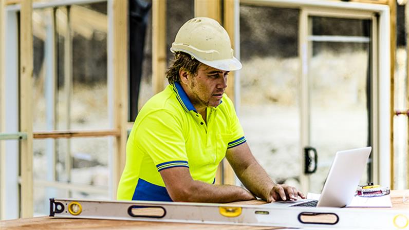 A photograph of a construction worker using a laptop