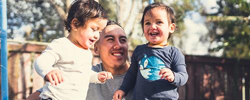 A photograph of a man with two toddlers outdoors