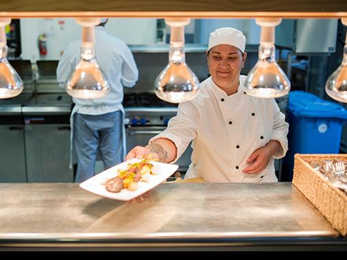 A chef delivering a meal for service in a commercial kitchen