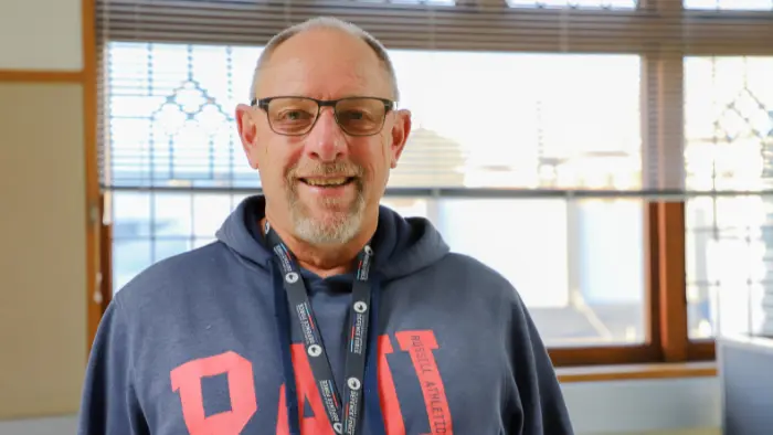 a man wearing glasses and a grey sweatshirt with red letters