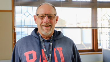 a man wearing glasses and a grey sweatshirt with red letters