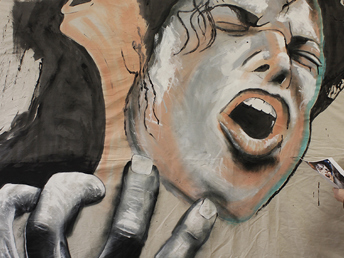 A large scale illustration on a wall with the artist standing next to it.