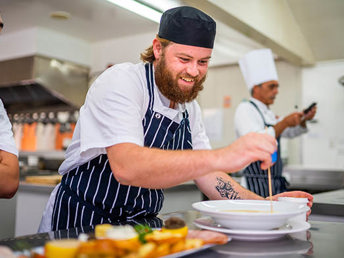 A UCOL cookery learner platting a dish in the kitchen