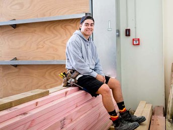 A carpentry student sitting on a pile of timber