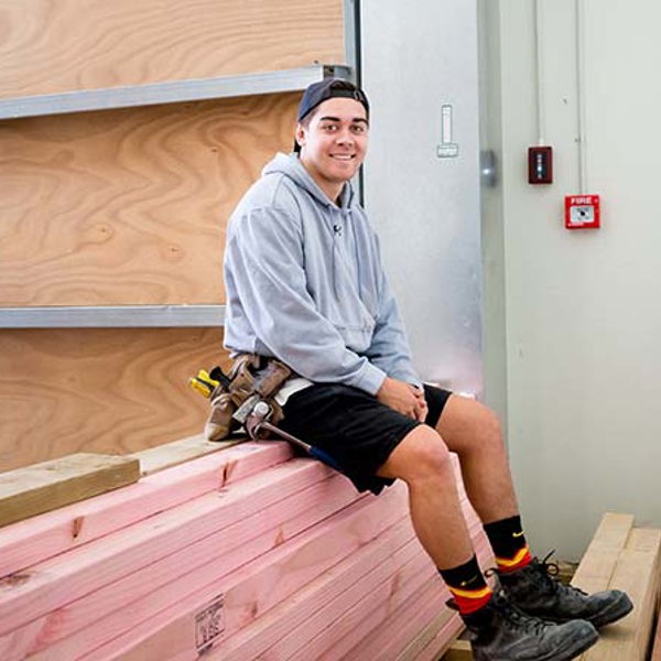 A carpentry student sitting on a pile of timber